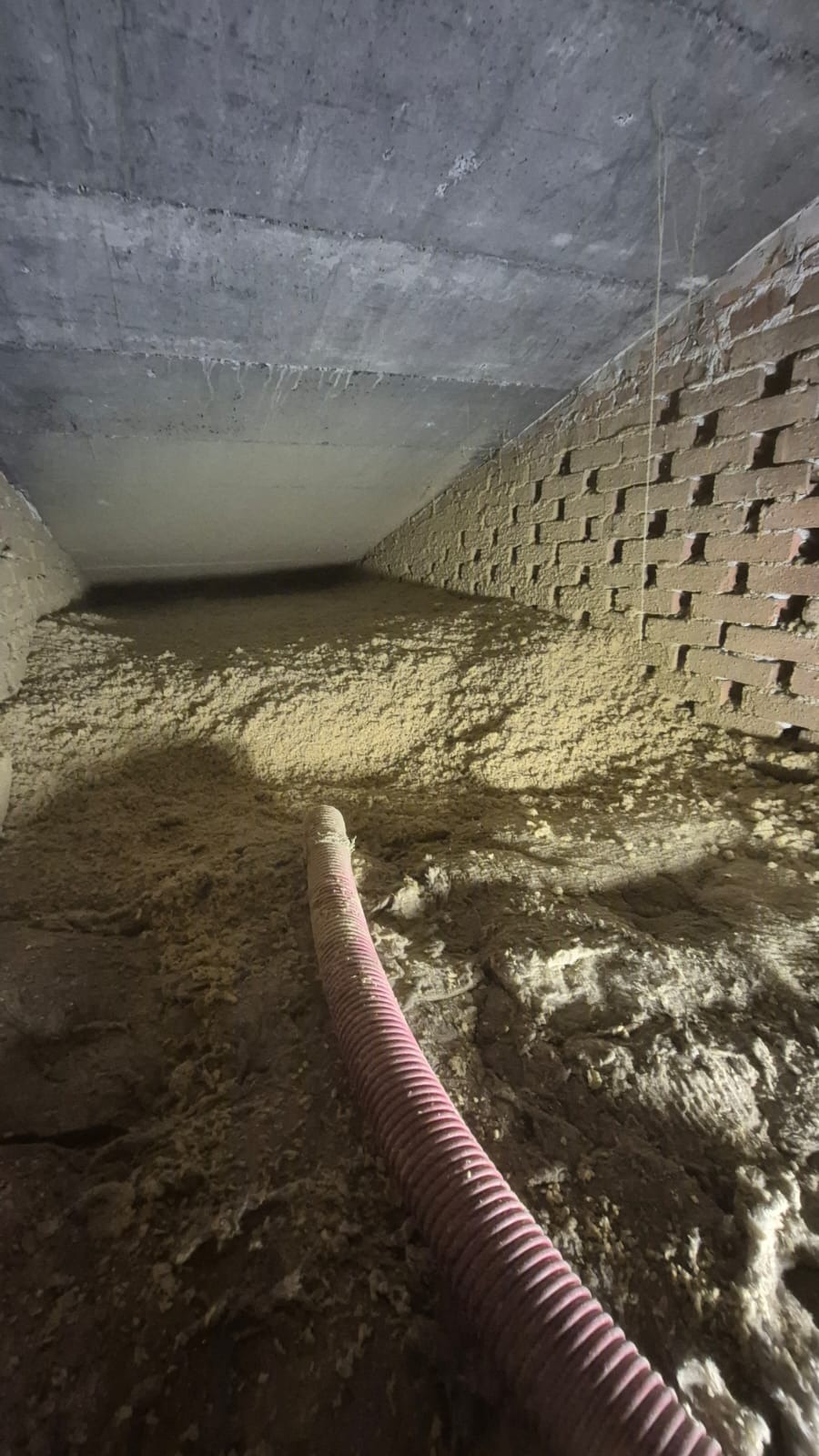 Aplikacja izolacji celulozowej w poddaszu w Tarnowskich Górach. Widoczny wąż aplikacyjny i wypełniona przestrzeń między ceglaną ścianą a betonowym stropem.