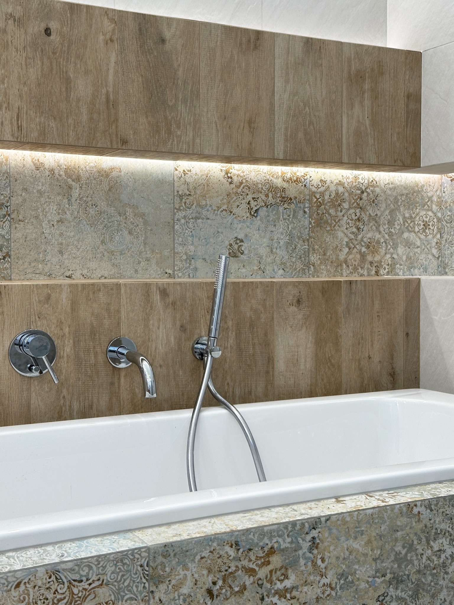 Biała wanna z chromowaną armaturą i prysznicem, obudowana płytkami w stylu rustykalnym z podświetleniem LED, element wystroju łazienki.