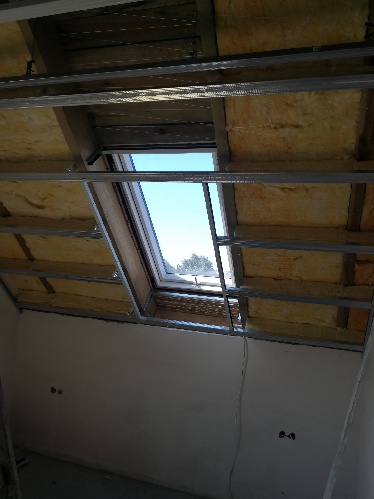 Montaż izolacji z wełny mineralnej i metalowego rusztu pod płytę gipsowo-kartonową na poddaszu z oknem dachowym.