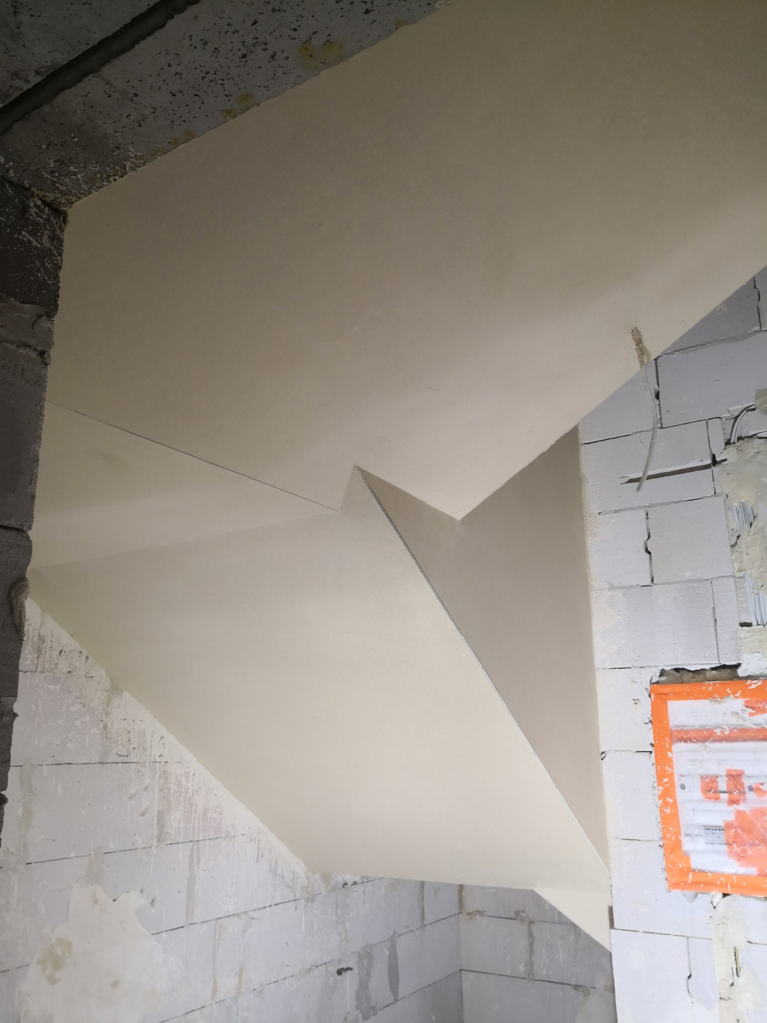 Wykończone, jasne poddasze ze skośnym sufitem, widoczne surowe ściany z białego bloczka i zabezpieczona instalacja elektryczna.