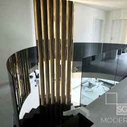 SG Modern Grzegorz Stopka - Nowoczesne schody spiralne z metalowymi balustradami i szklanymi panelami, oświetlone kolumny dekoracyjne, widok z góry na salon z białymi meblami.