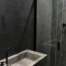 SG Modern Grzegorz Stopka - Nowoczesna łazienka z kabiną prysznicową typu walk-in, umywalką z kamienia i czarną armaturą na tle ciemnych, grafitowych płytek. Minimalistyczny design.