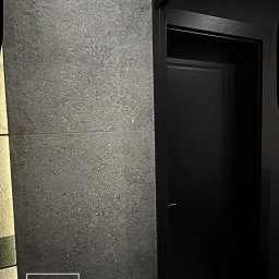 SG Modern Grzegorz Stopka - Minimalistyczne wnętrze: ciemnoszara ściana z płytek imitujących kamień, czarne drzwi wewnętrzne z ościeżnicą. Nowoczesny design z dbałością o detale.
