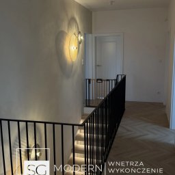 SG Modern Grzegorz Stopka - Nowoczesne wnętrze: schody z podświetleniem LED, czarna balustrada, parkiet w jodełkę. Na ścianie okrągły kinkiet z ażurowym kloszem. Minimalistyczny design.