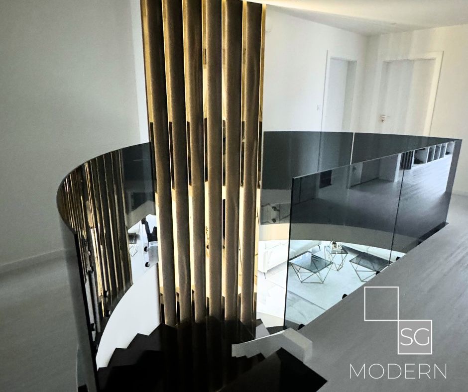 Nowoczesne schody spiralne z metalowymi balustradami i szklanymi panelami, oświetlone kolumny dekoracyjne, widok z góry na salon z białymi meblami.