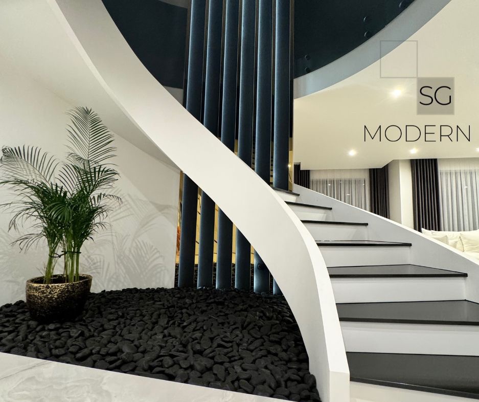 Nowoczesne wnętrze z krętymi schodami, dekoracyjnymi czarnymi kamieniami, rośliną doniczkową i pionowymi panelami w kolorze granatowym z elementami złota.