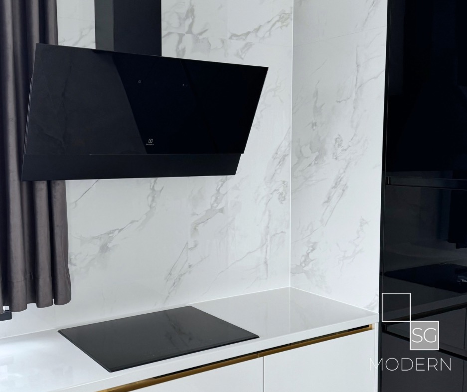 Nowoczesna kuchnia z czarnym okapem Electrolux i płytą indukcyjną na białym blacie z marmurowym tłem, wykończona złotymi detalami.