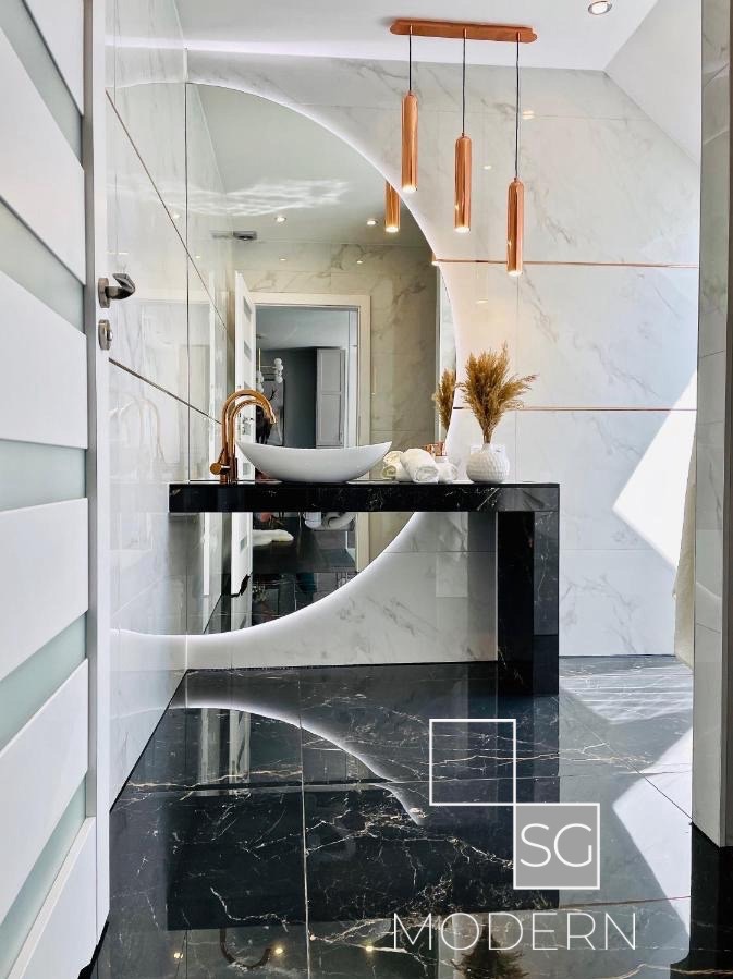 Nowoczesna łazienka z czarno-białą marmurową podłogą i ścianami, umywalką nablatową na czarnym blacie z podświetleniem LED i miedzianymi lampami wiszącymi.
