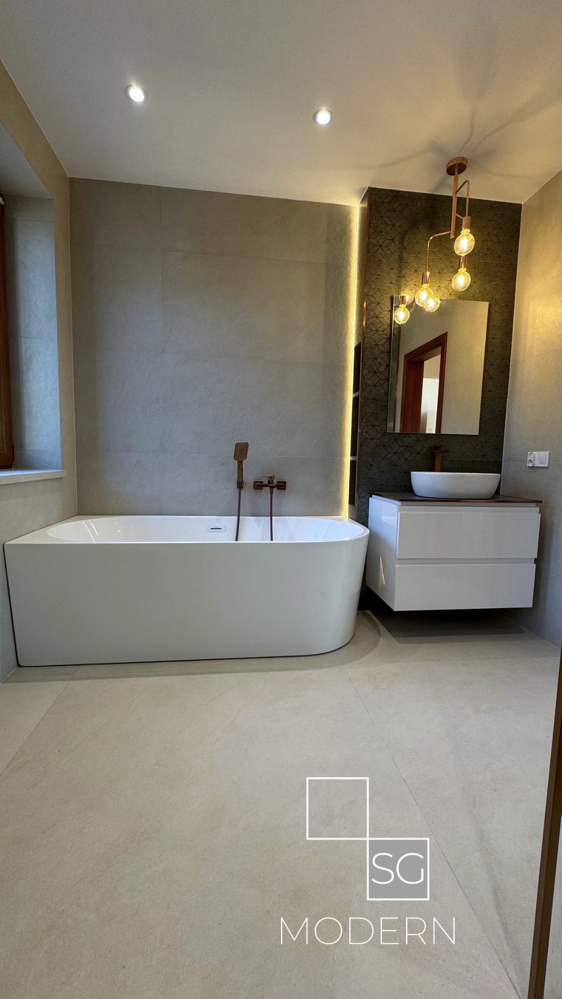 Nowoczesna łazienka z wolnostojącą wanną, umywalką nablatową na szafce, lustrem z podświetleniem LED i baterią w kolorze miedzi.