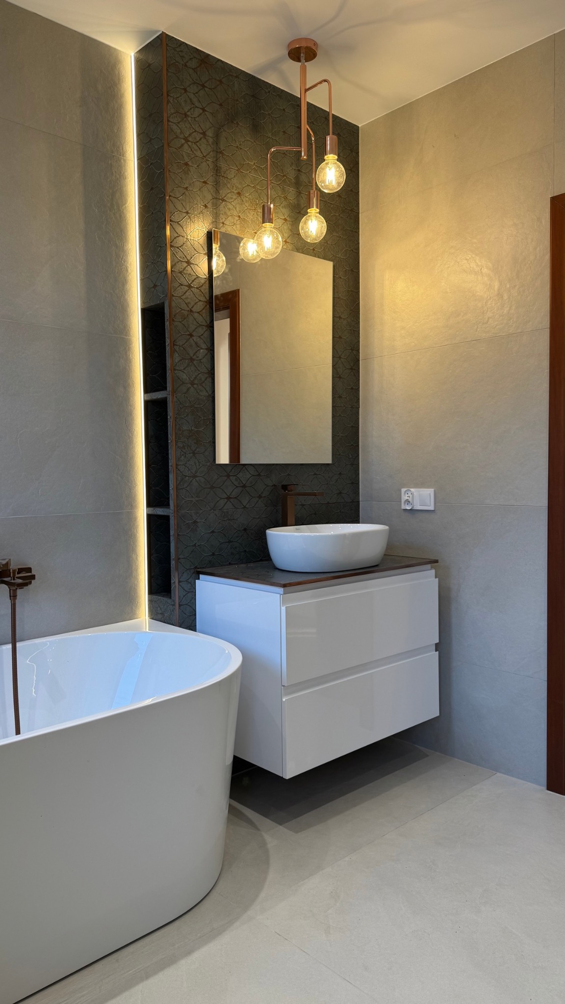 Nowoczesna łazienka z wolnostojącą wanną, białą szafką z umywalką nablatową, lustrem i dekoracyjną lampą w kolorze miedzi.