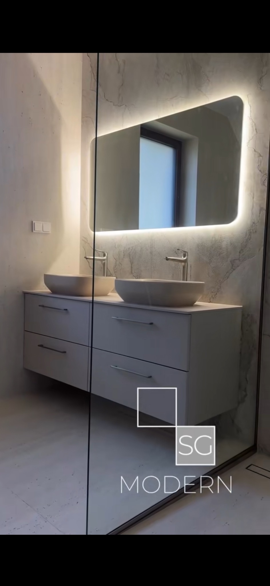 Nowoczesna łazienka z podwójną umywalką nablatową, szafką z szufladami i podświetlanym lustrem. Minimalistyczny design, marmurowe ściany, szklana kabina prysznicowa.