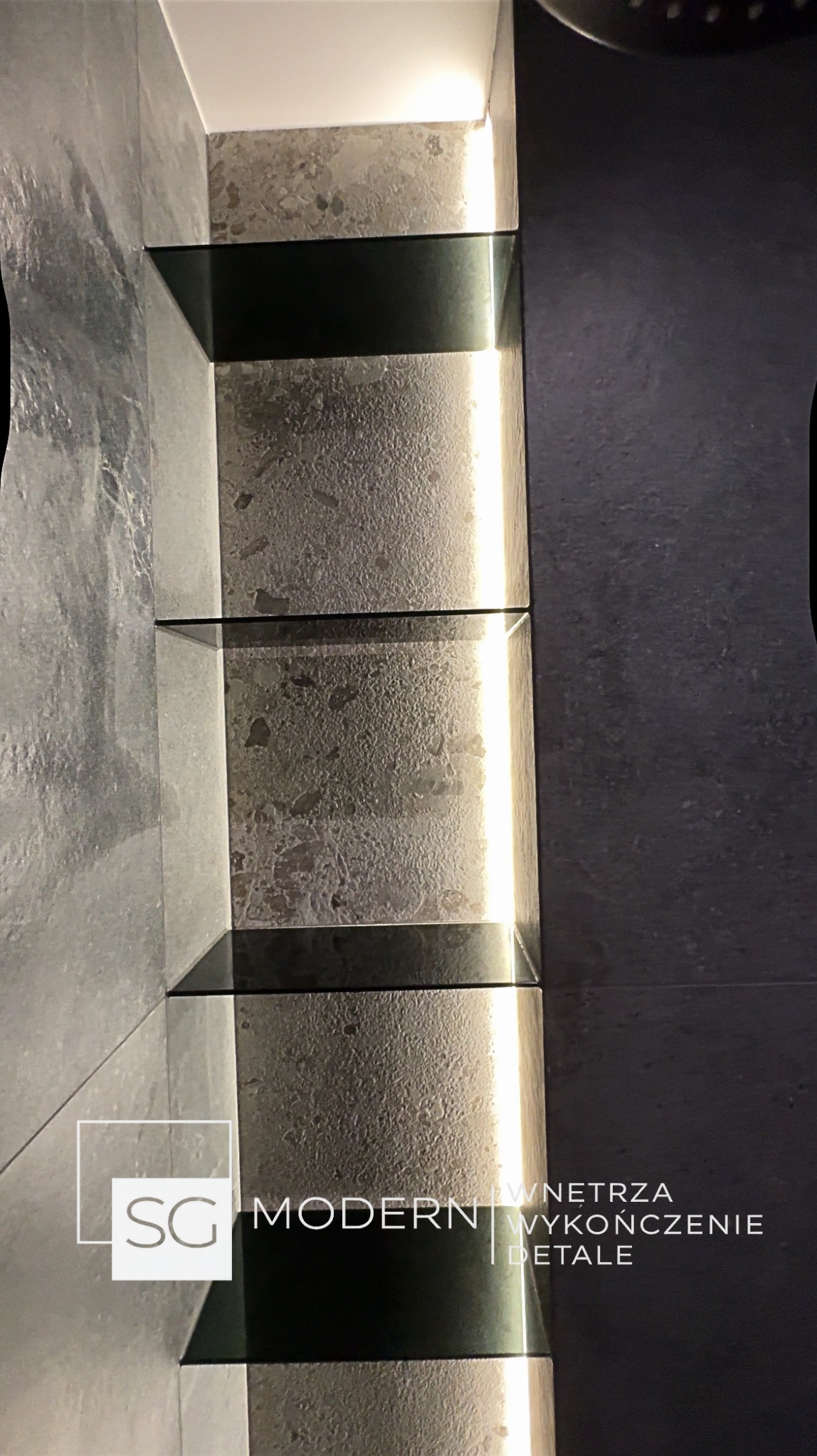 Szczegółowe ujęcie nowoczesnej łazienki z podświetlanymi półkami z ciemnego szkła, na tle szarej, teksturowanej ściany. Minimalistyczny design z dbałością o detale.