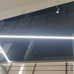 Tom-Kaj - Sufit podwieszany z czarną przestrzenią i geometrycznym oświetleniem LED, widok z dołu, fragment rusztowania po prawej stronie.