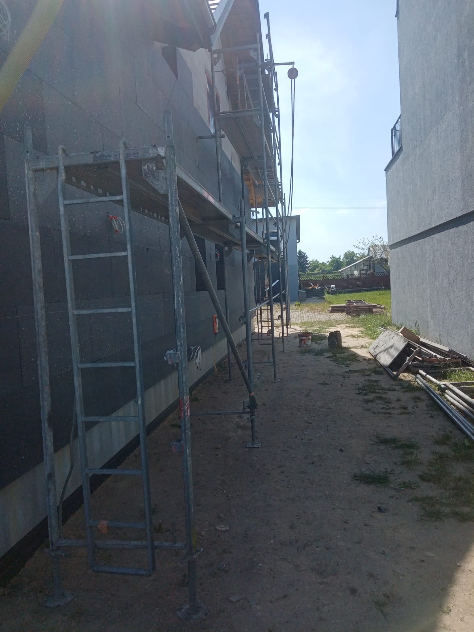 Elewacja budynku w trakcie ocieplania styropianem grafitowym, widoczne rusztowania i teren budowy.