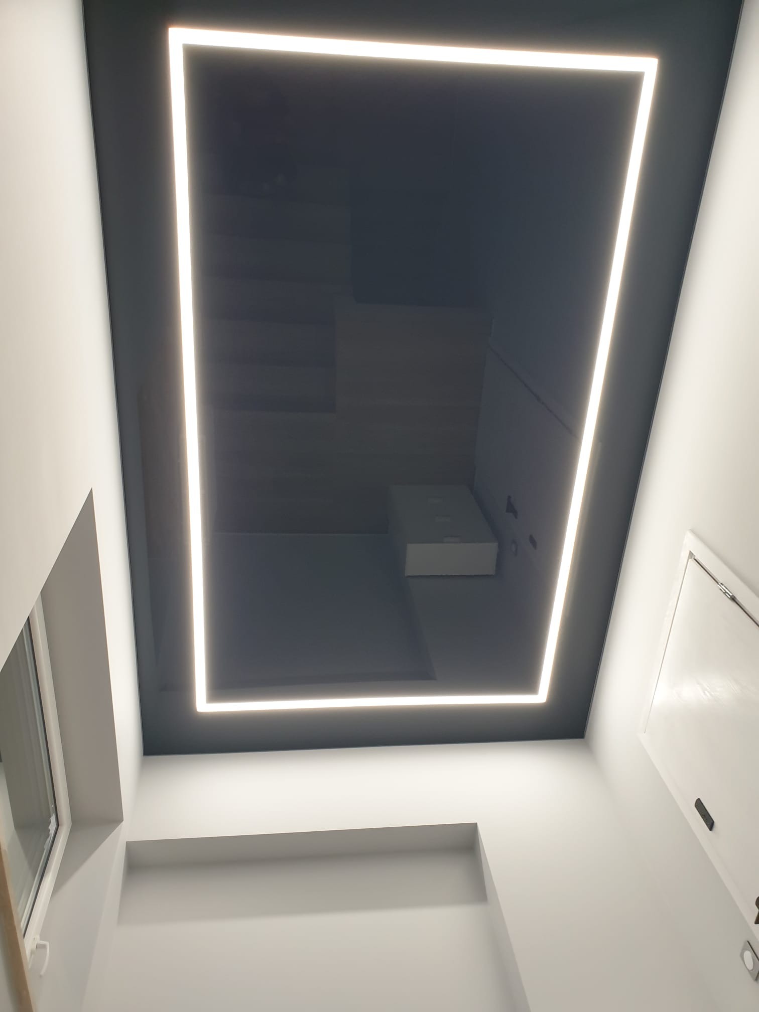 Czarny, lustrzany sufit z kwadratowym oświetleniem LED w nowoczesnym wnętrzu, widok z dołu.