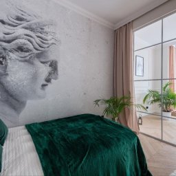 Oleksandr Nazarow - Sypialnia z dekoracyjną ścianą z motywem rzeźby, zielonym pledem na łóżku i przeszkloną ścianą działową z widokiem na salon