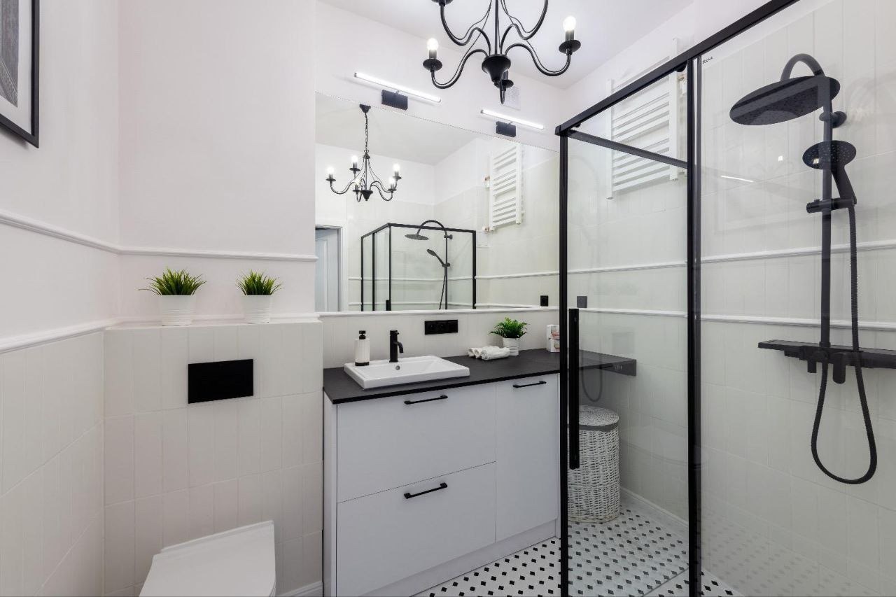 Nowoczesna łazienka w bieli i czerni z kabiną prysznicową typu walk-in, umywalką nablatową na szafce z szufladami i dekoracyjnym żyrandolem.