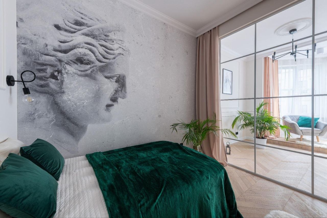 Sypialnia z dekoracyjną ścianą z motywem rzeźby, zielonym pledem na łóżku i przeszkloną ścianą działową z widokiem na salon