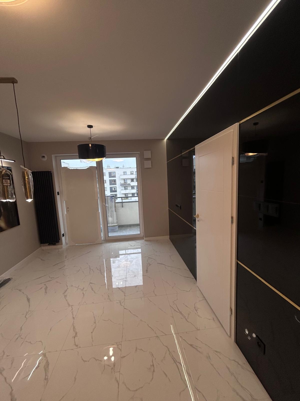 Nowoczesne wnętrze w Warszawie z marmurową podłogą, otwartymi drzwiami balkonowymi i oświetleniem LED wzdłuż sufitu, ukazujące efekt po remoncie.