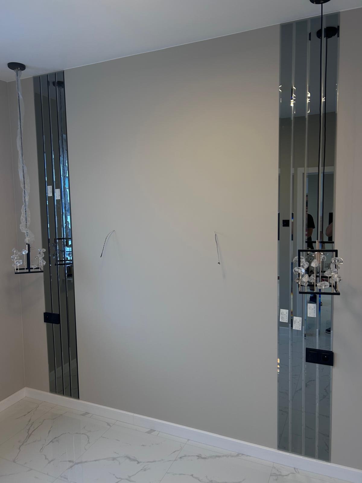 Montaż dekoracyjnych paneli lustrzanych po bokach ściany, widoczne wystające kable od lamp, podłoga wyłożona płytkami imitującymi marmur.