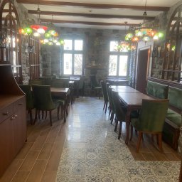 HUGO INVESTMENTS SPÓŁKA Z OGRANICZONĄ ODPOWIEDZIALNOŚCIĄ - Wnętrze restauracji z kamiennymi ścianami, drewnianymi belkami stropowymi, mozaikową podłogą i kolorowymi lampami wiszącymi.