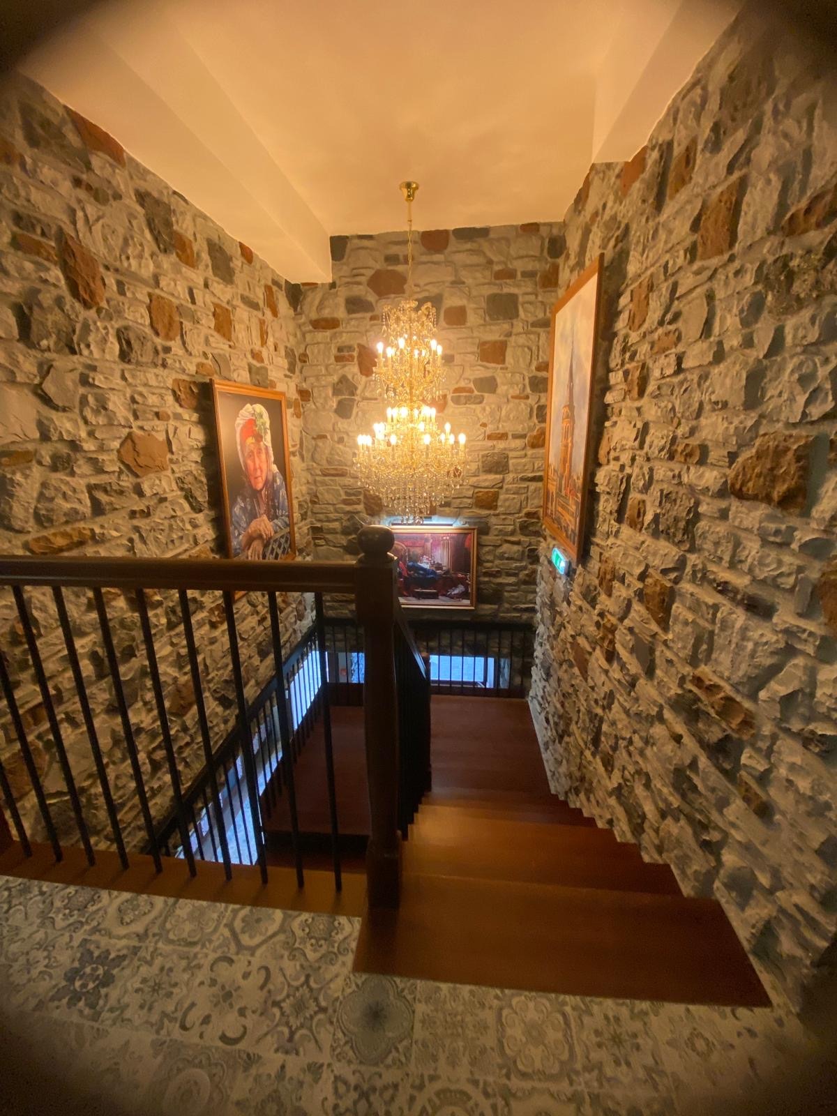 Kamienne ściany klatki schodowej z drewnianymi stopniami, oświetlone kryształowym żyrandolem i dekorowane obrazami, widok z góry.