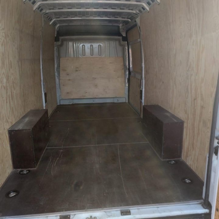 Wnętrze furgonetki wyłożone sklejką, z dodatkowymi skrzyniami po bokach, przygotowane do transportu towarów.