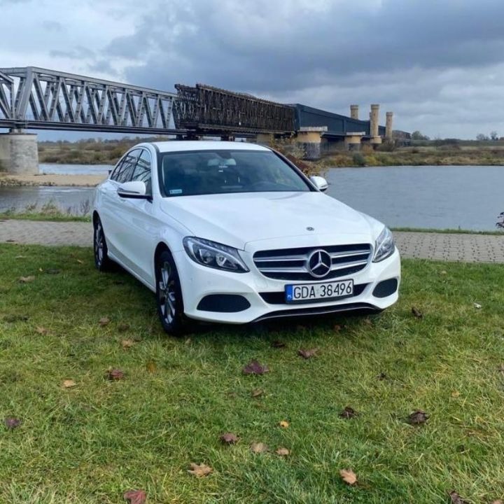 Biały Mercedes C-klasa z numerem rejestracyjnym GDA 36496 zaparkowany na trawie, w tle rzeka i most kolejowy.