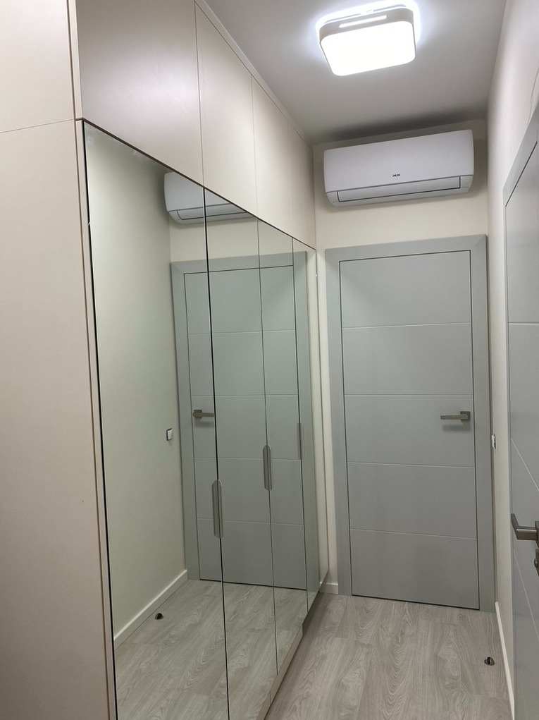 Szafa na wymiar z lustrzanymi drzwiami w przedpokoju, odbijająca drzwi wejściowe i klimatyzator na ścianie.