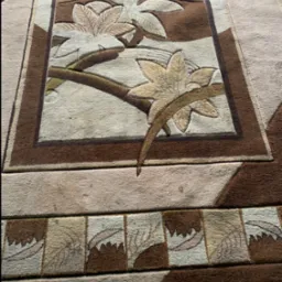 Beżowo-brązowy dywan z motywem liści, widoczne detale wzoru i faktury materiału, delikatne cieniowanie.