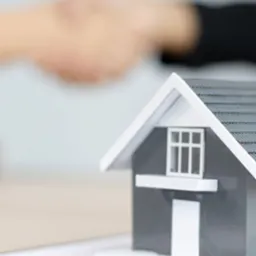 Model domu z kluczami na umowie, w tle uścisk dłoni.