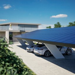 STARK SPÓŁKA Z OGRANICZONĄ ODPOWIEDZIALNOŚCIĄ - Nowoczesna wiata garażowa z panelami słonecznymi nad dwoma białymi samochodami sportowymi, na tle minimalistycznego domu z balkonem i błękitnego nieba.