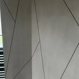 Dekoracyjna ściana wewnętrzna z szarą, teksturowaną powierzchnią i czarnymi, geometrycznymi liniami, widok z narożnika pomieszczenia, fragment drewnianej podłogi.