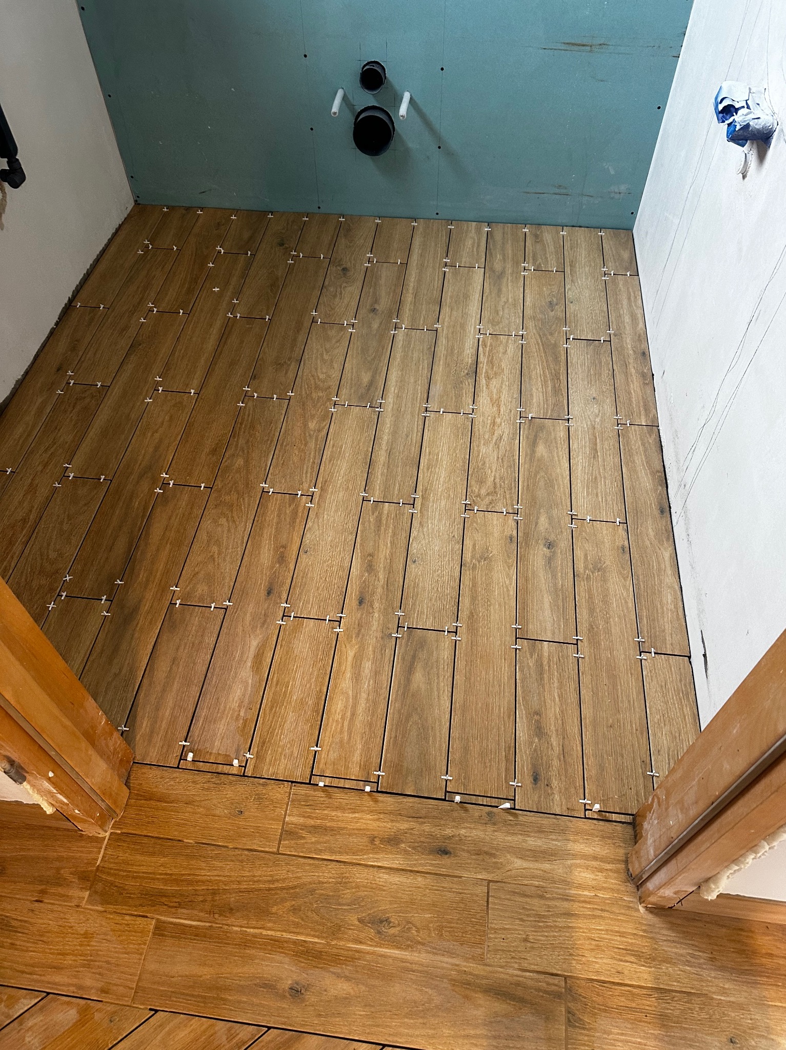 Układanie podłogi z płytek imitujących drewno w trakcie prac w łazience, widoczne krzyżyki dystansowe, surowe ściany przygotowane do dalszych prac wykończeniowych.