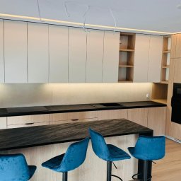 Dopasowany Studio - Nowoczesna kuchnia z drewnianymi szafkami, czarnym blatem i wyspą z trzema turkusowymi hokerami, oświetlenie LED pod szafkami wiszącymi i na suficie.