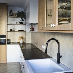 Dopasowany Studio - Nowoczesna kuchnia z białymi szafkami, czarnym blatem i armaturą, drewnianymi szafkami wiszącymi z przeszklonymi frontami oraz drewnianą podłogą ułożoną w jodełkę.