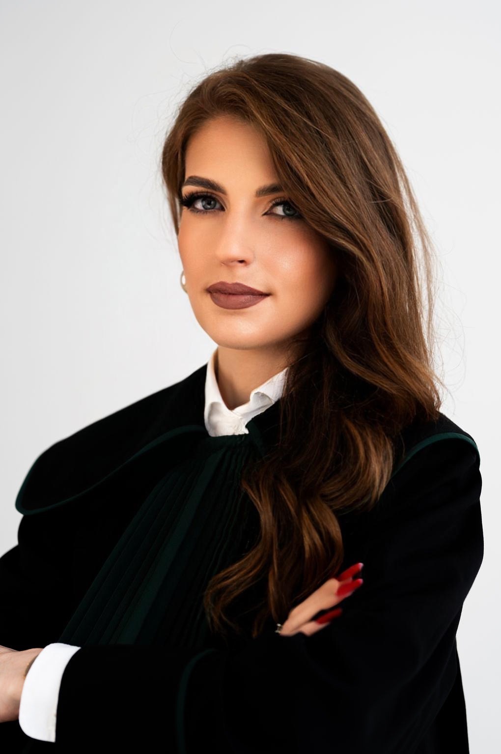 Portret kobiety adwokat w todze, z założonymi rękami, na jasnym tle.