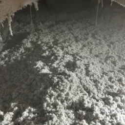 Szczegółowe ujęcie izolacji z wełny mineralnej w przestrzeni poddasza, z widocznymi elementami konstrukcyjnymi i przewodami. Jasne, rozproszone światło.