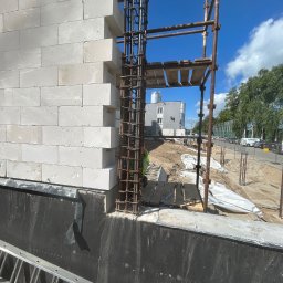 BAR-KAM GROUP SP. Z O.O - Wznoszenie ściany z bloczków betonu komórkowego Ytong z widocznym zbrojeniem pionowym i rusztowaniem. Prace murarskie w toku na tle błękitnego nieba.