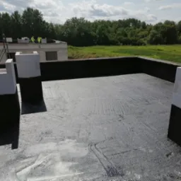 Budowa domu z betonu komórkowego: widok z góry na izolowany fundament i wznoszone ściany. W tle zieleń i pracownicy na kolejnym etapie budowy.