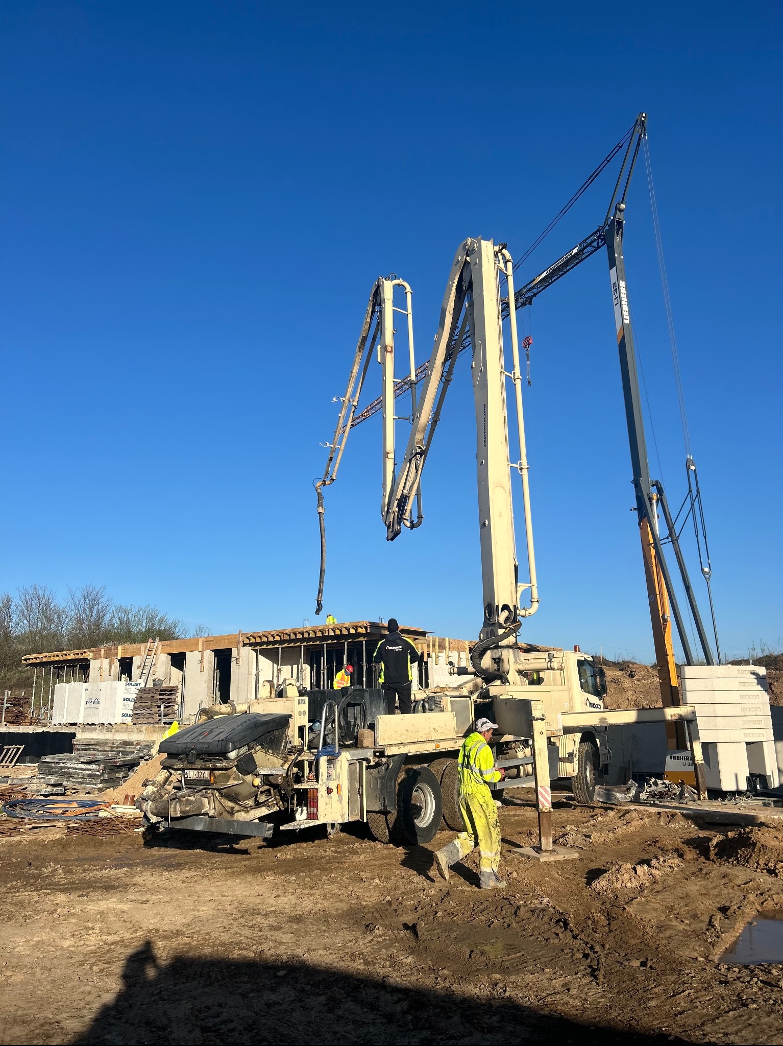 Betonowanie stropu domu jednorodzinnego przy użyciu pompy do betonu Liebherr; pracownicy w ubraniach roboczych nadzorują proces w słoneczny dzień.