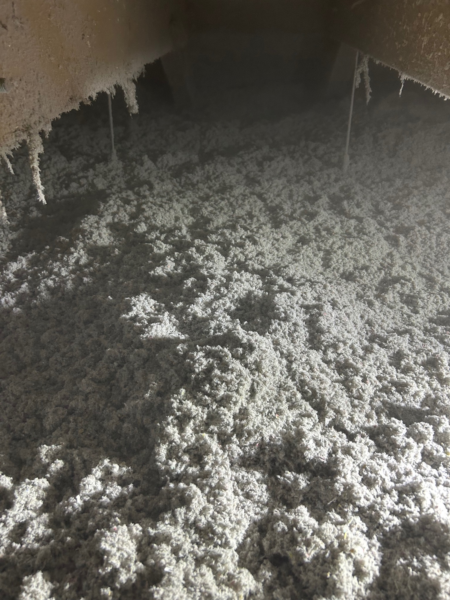 Szczegółowe ujęcie izolacji z wełny mineralnej w przestrzeni poddasza, z widocznymi elementami konstrukcyjnymi i przewodami. Jasne, rozproszone światło.