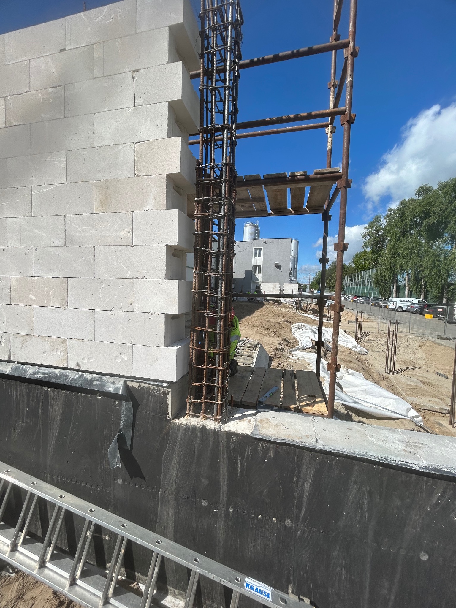 Wznoszenie ściany z bloczków betonu komórkowego Ytong z widocznym zbrojeniem pionowym i rusztowaniem. Prace murarskie w toku na tle błękitnego nieba.