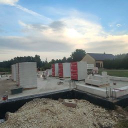 Fasadecraft - Budowa domu jednorodzinnego: fundamenty zbrojone, bloczki Termobet, widok na plac budowy w trakcie wznoszenia ścian. Niebo z chmurami w tle.
