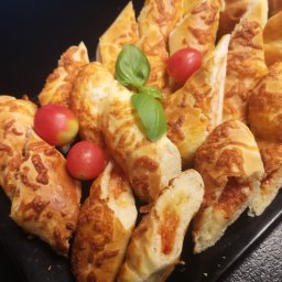 Food Miód i Orzeszki - Kawałki pieczywa z serem i pomidorami na czarnym talerzu, udekorowane listkami bazylii i pomidorkami koktajlowymi.