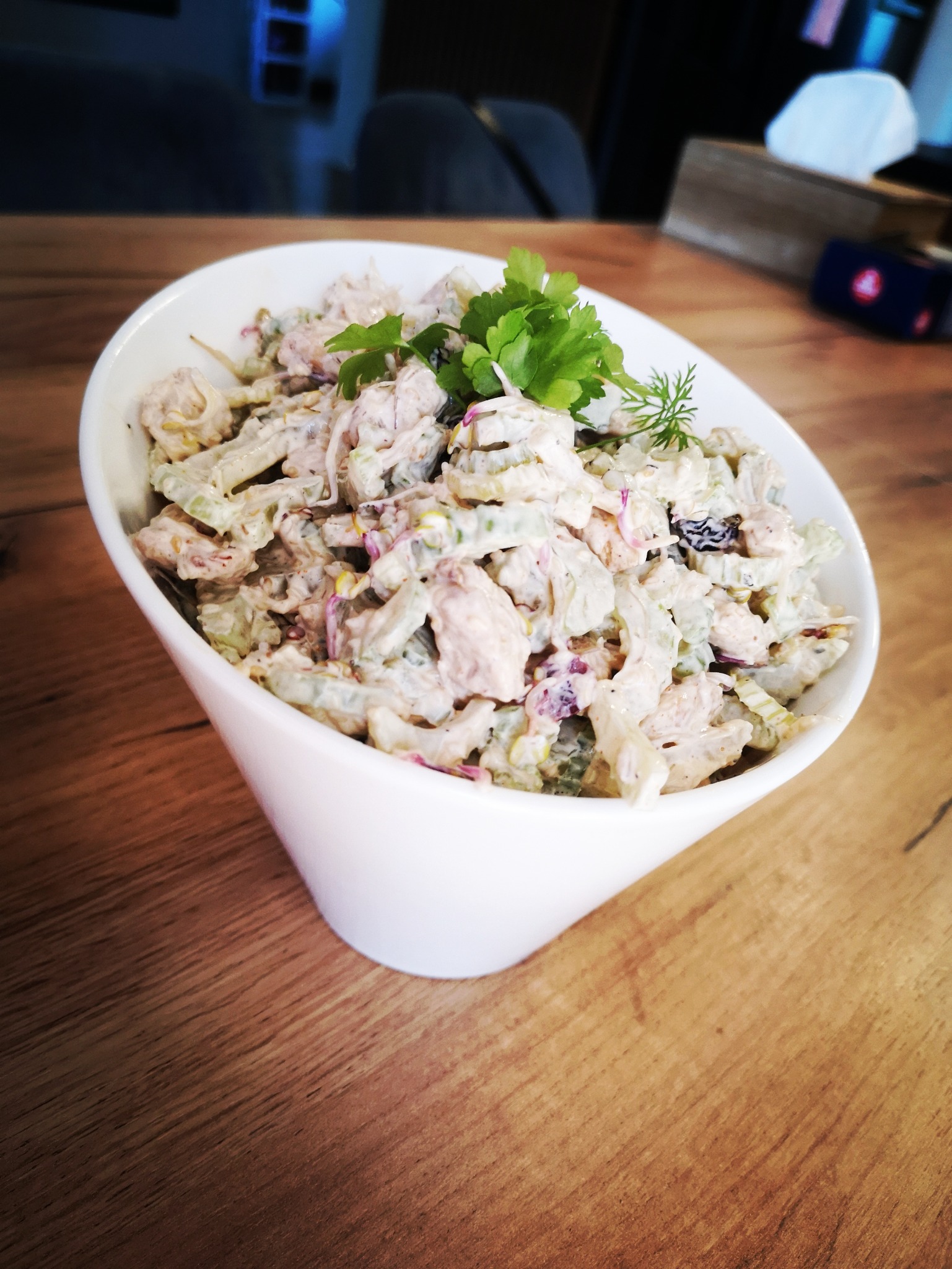 Sałatka jarzynowa z majonezem i ziołami w białej misce na drewnianym stole, widok z góry.