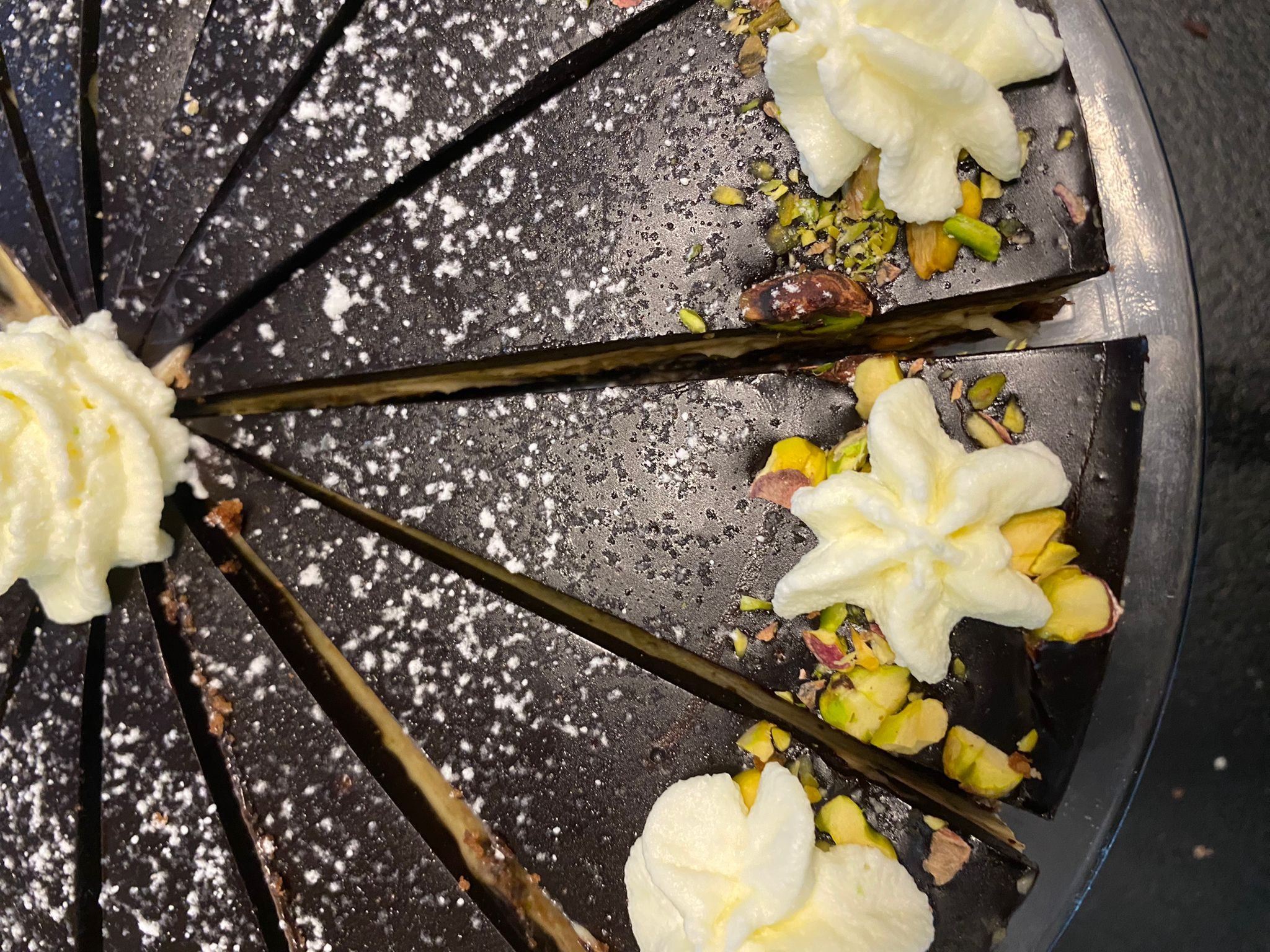 Kawałki tortu czekoladowego posypane cukrem pudrem i udekorowane bitą śmietaną oraz pistacjami, widok z góry.