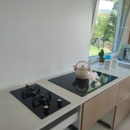 Pyk Pyk Elektryk - Nowoczesna kuchnia w Chabówce z zamontowaną płytą indukcyjną i gazową, czajnik ceramiczny na blacie. Ujęcie z otwartą szufladą pod płytą indukcyjną.