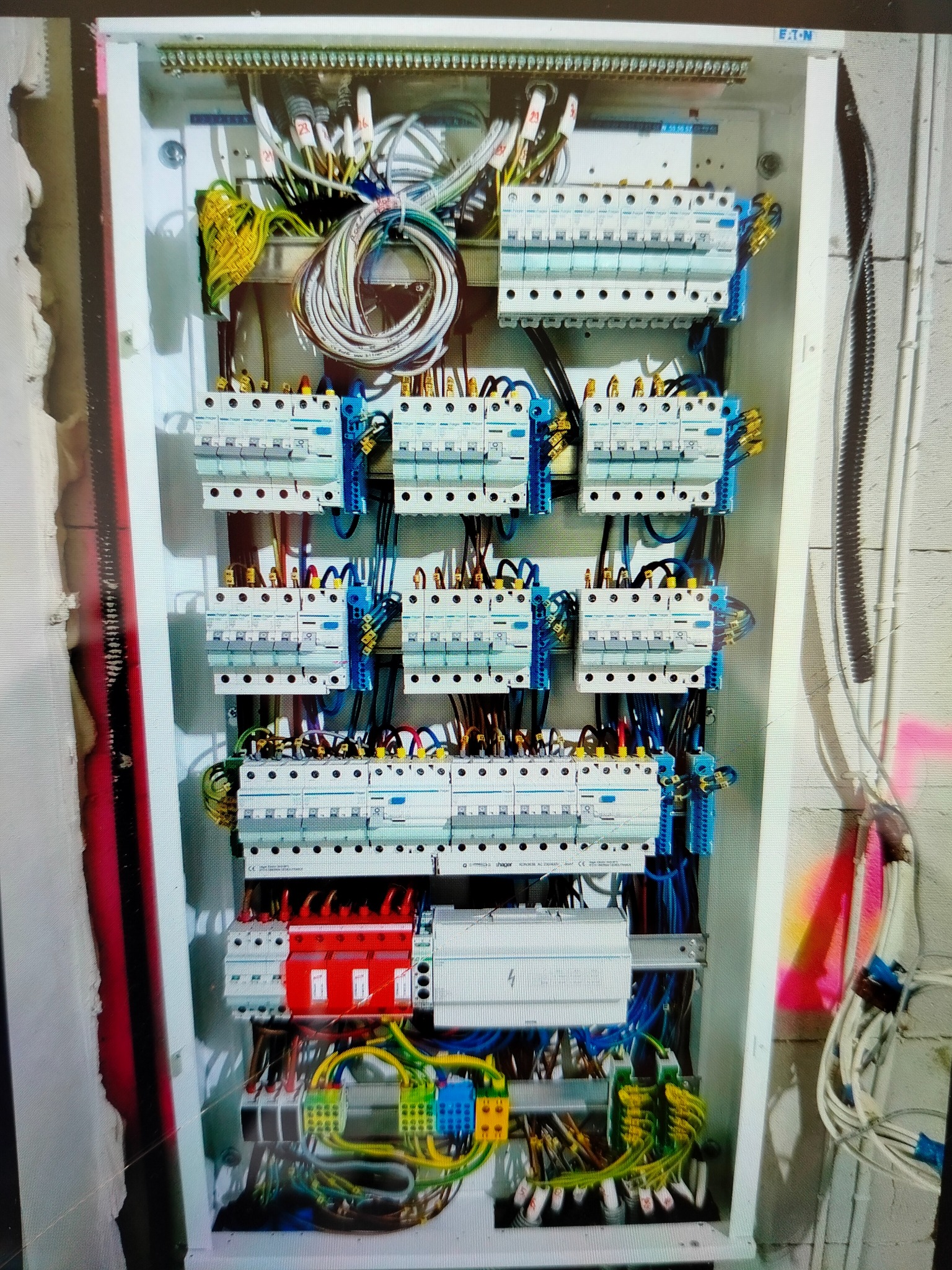 Rozdzielnica elektryczna z bezpiecznikami, okablowaniem i zabezpieczeniami przeciwprzepięciowymi, widoczne kable w różnych kolorach, szyna DIN oraz elementy montażowe wewnątrz obudowy, ściana...
