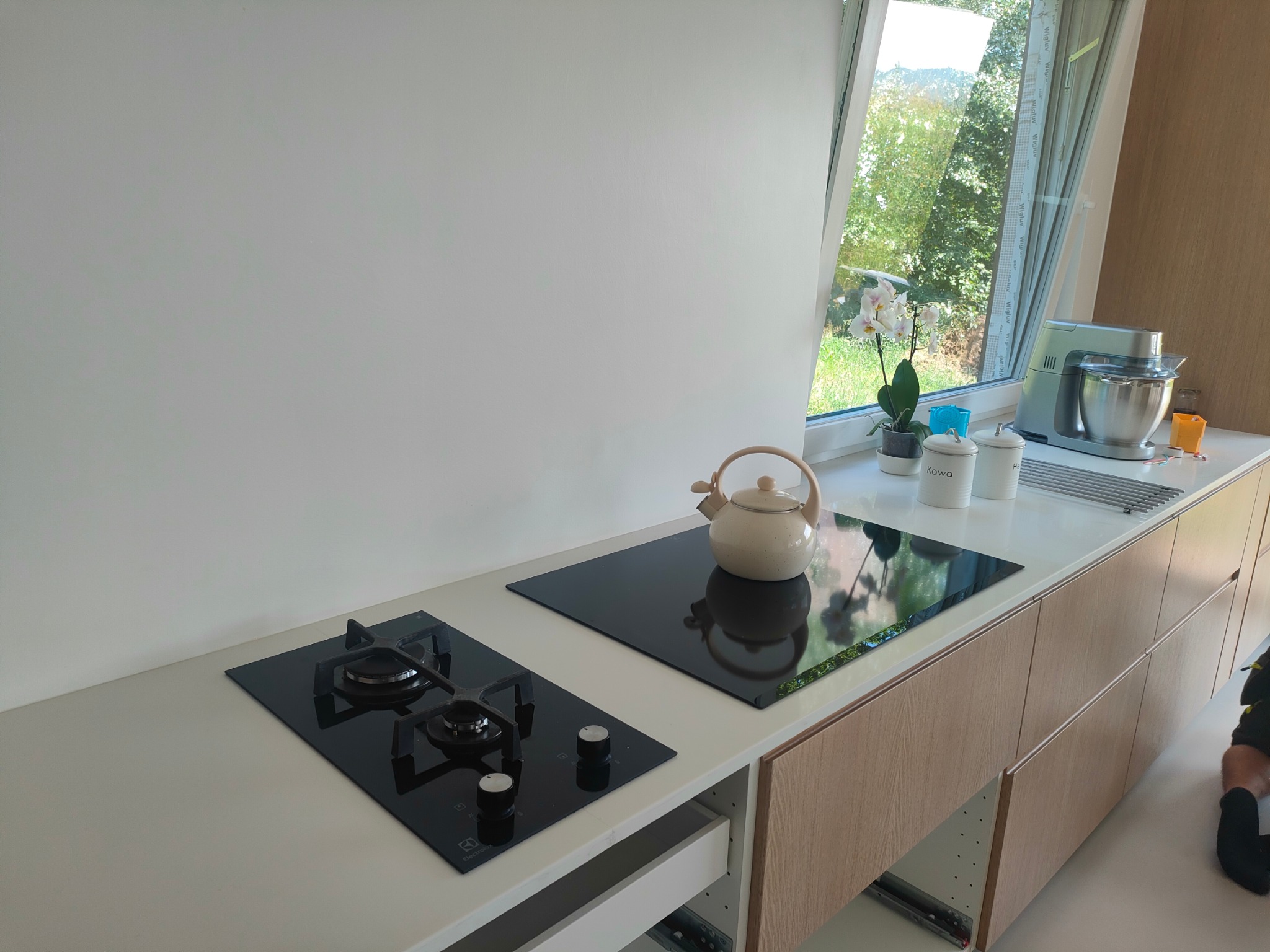 Nowoczesna kuchnia w Chabówce z zamontowaną płytą indukcyjną i gazową, czajnik ceramiczny na blacie. Ujęcie z otwartą szufladą pod płytą indukcyjną.